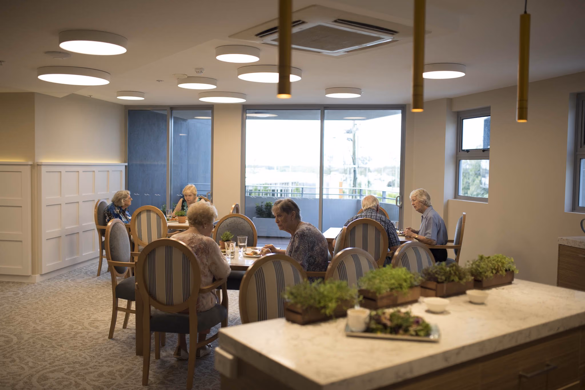 Residents at lunch in the household's dining room, with the windows behind them